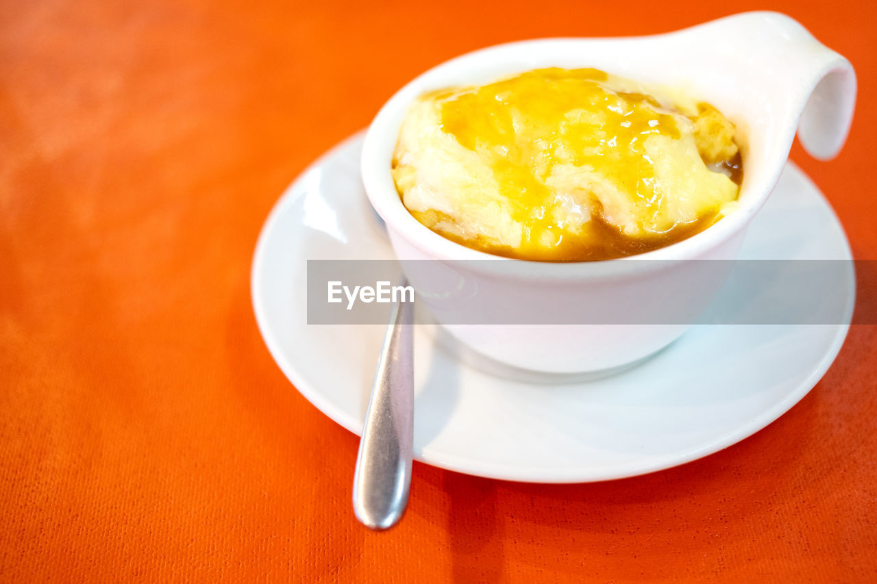 A cup of mashed potato and cheese on top with spoon put on red table background