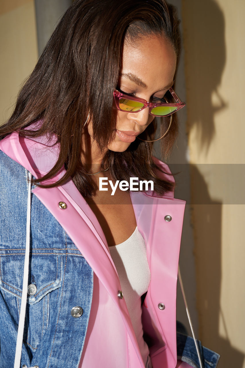 CLOSE-UP OF YOUNG WOMAN WEARING SUNGLASSES STANDING AGAINST PINK OUTDOORS