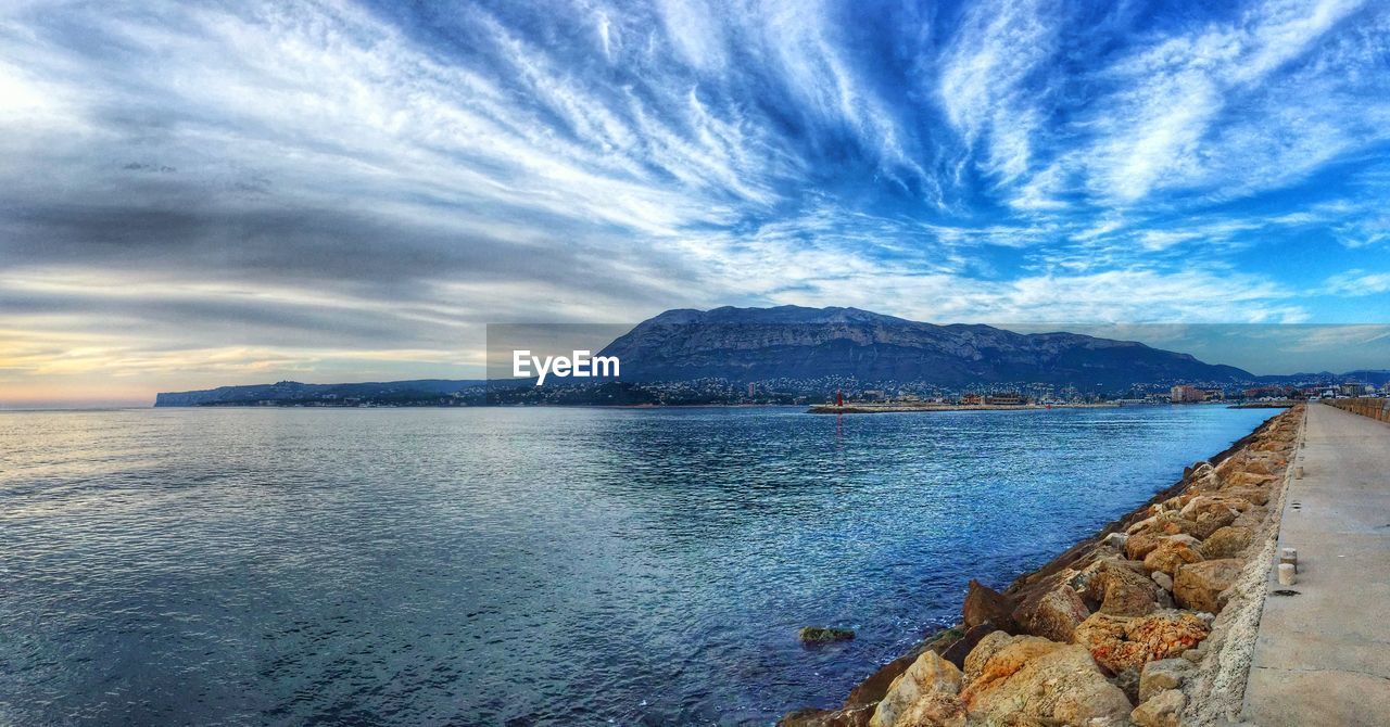 SCENIC VIEW OF SEA AND MOUNTAIN AGAINST CLOUDY SKY