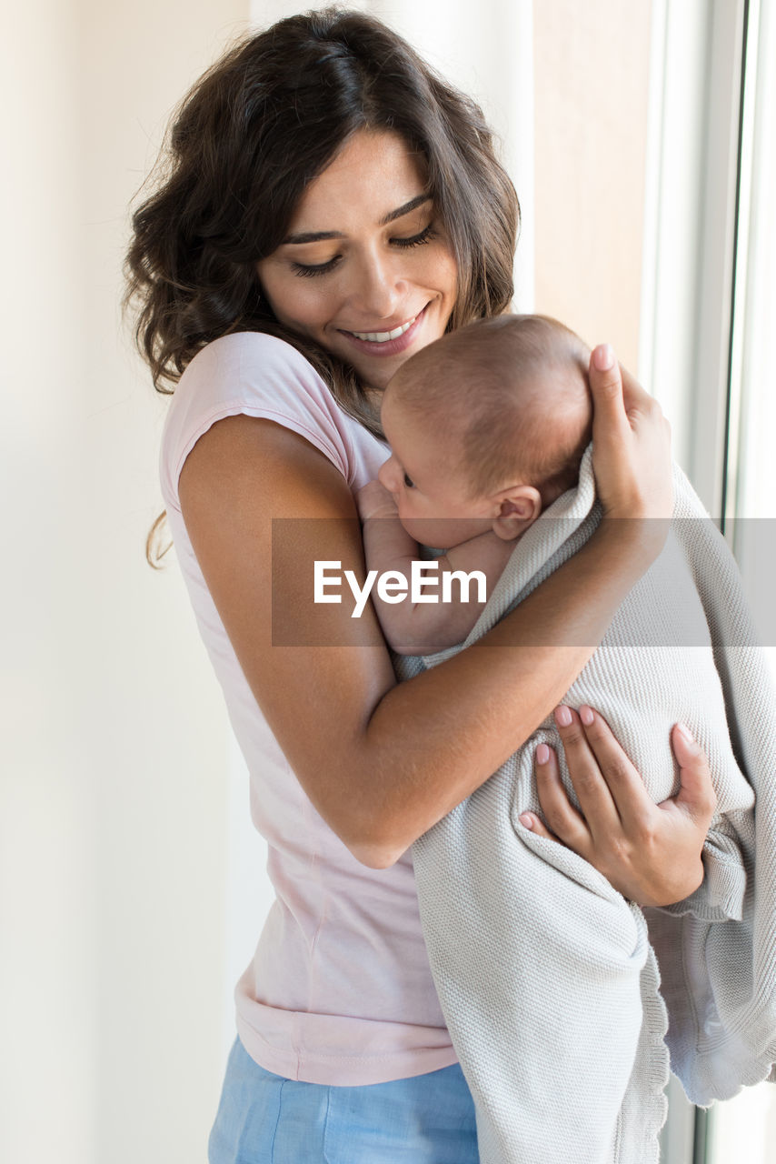 Smiling mother carrying cute daughter at home