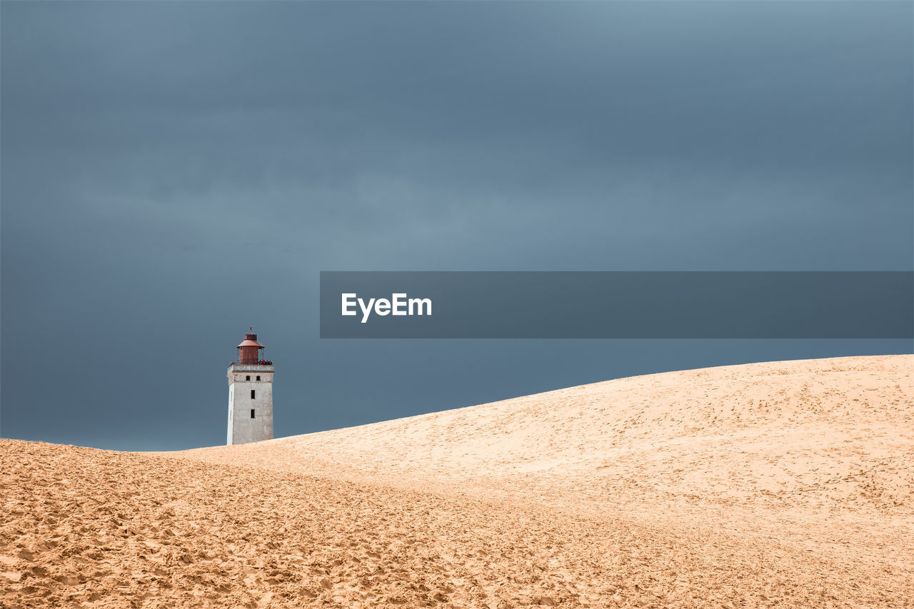 Lighthouse on beach by building against sky