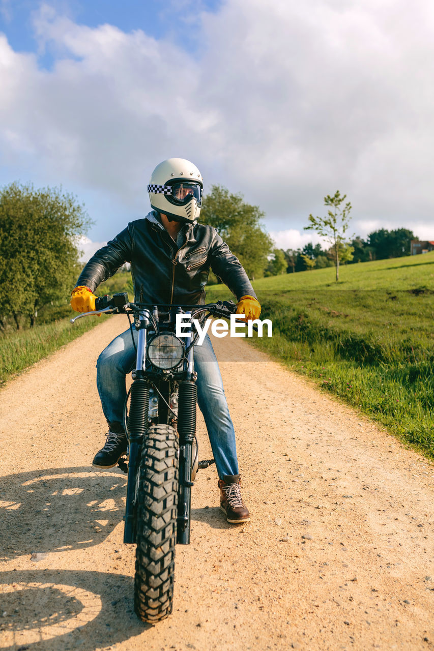 Man riding motorcycle on dirt road against sky