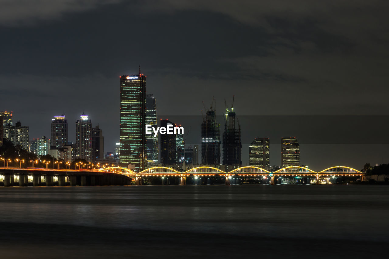 Illuminated city by river against sky at night