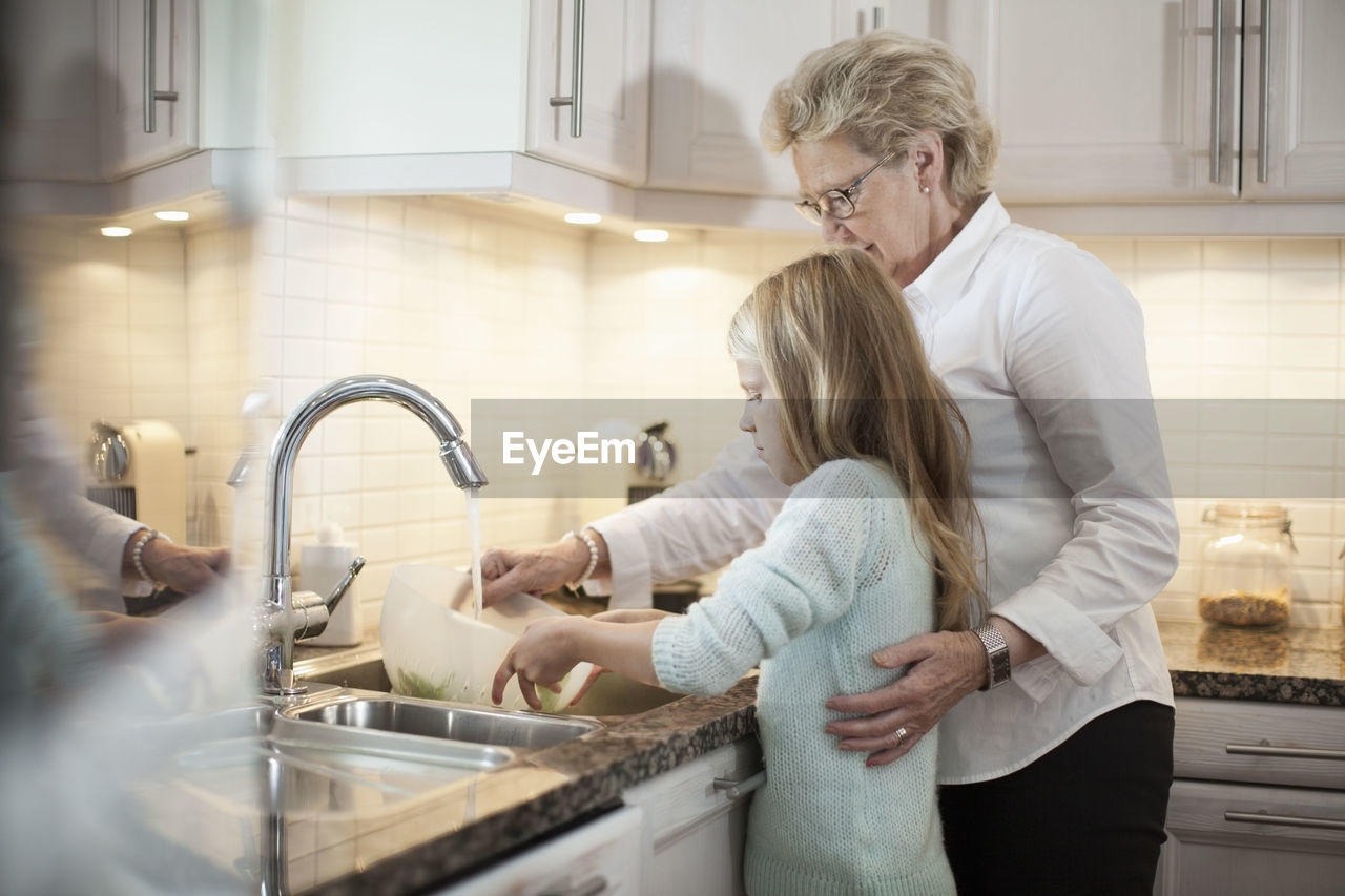 Grandmother and granddaughter washing vegetables in kitchen