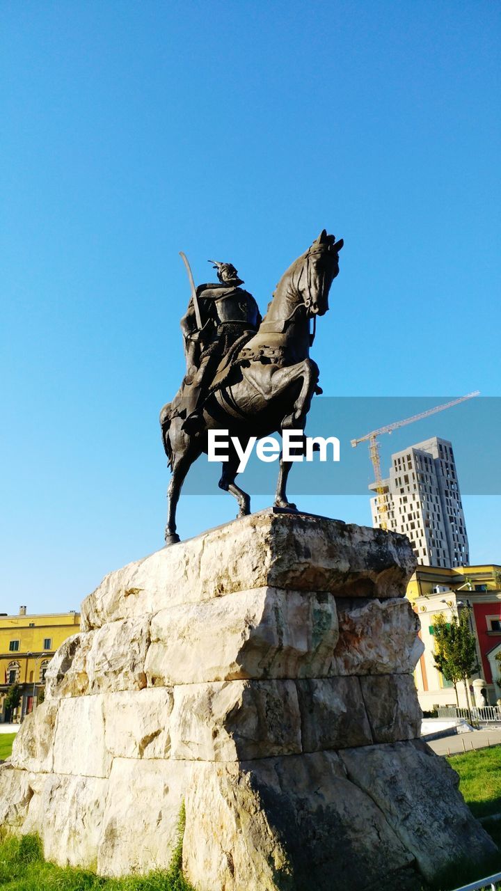 LOW ANGLE VIEW OF STATUE PERCHING ON ROCK AGAINST SKY