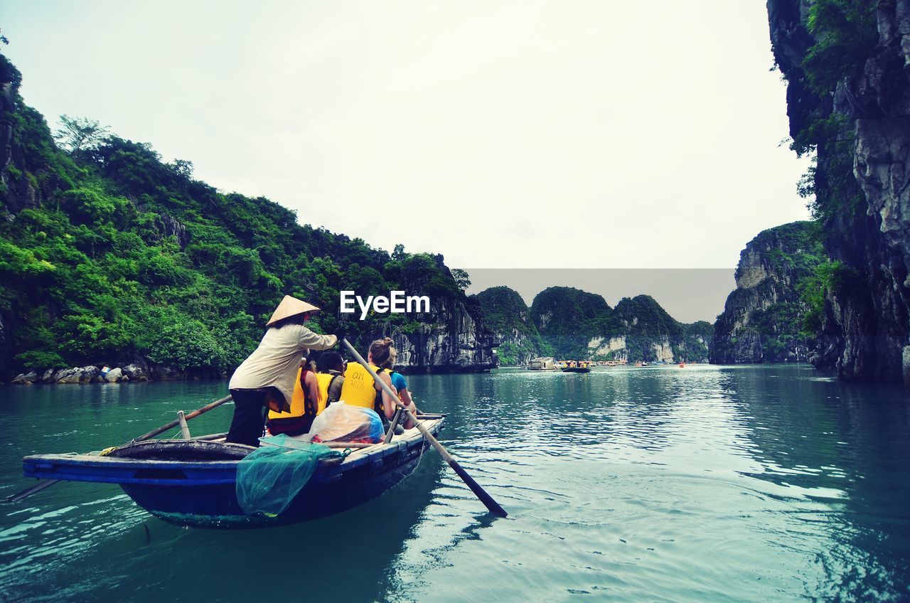 People boating in calm sea against lush foliage