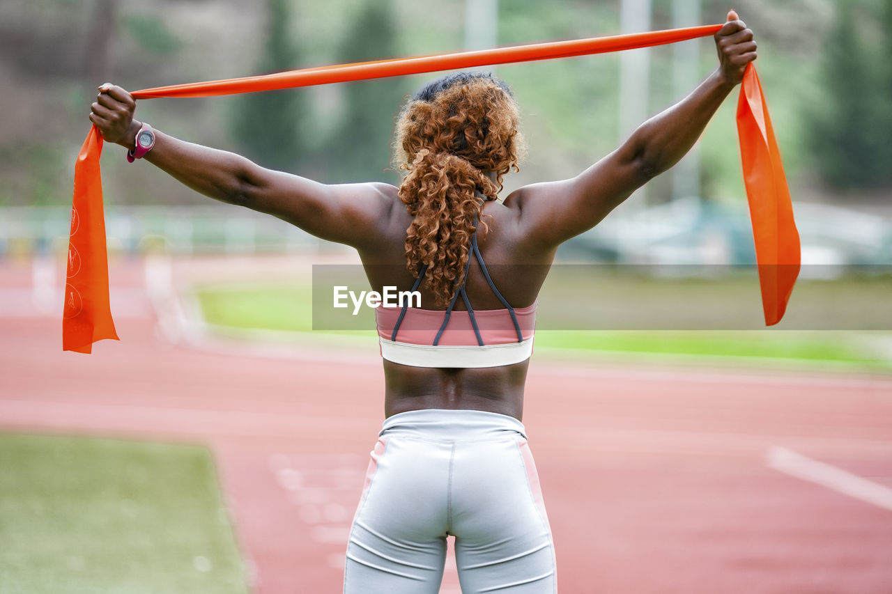 Sportswoman stretching resistance band while standing on running track