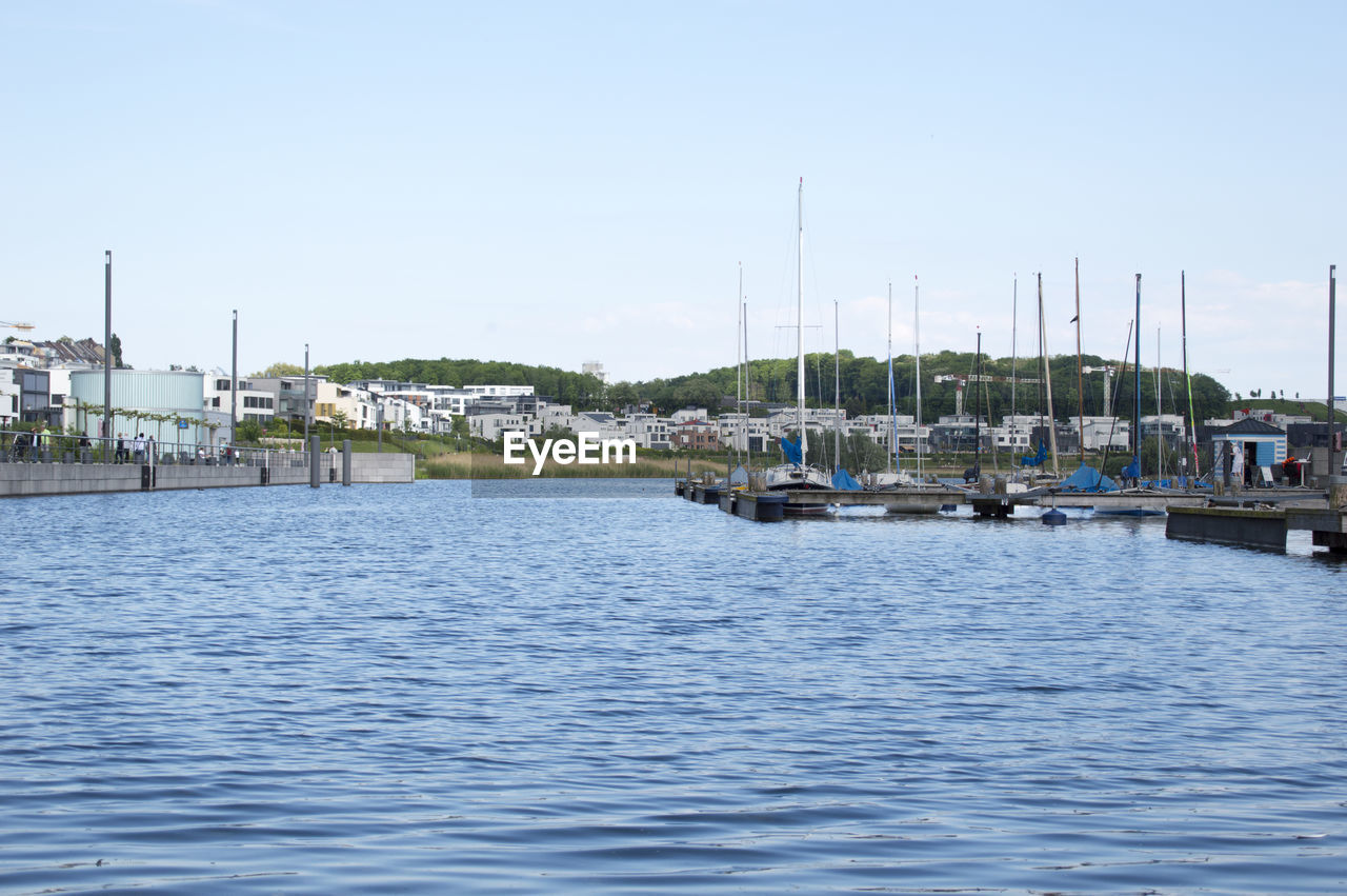 SAILBOATS MOORED ON HARBOR AGAINST CLEAR SKY