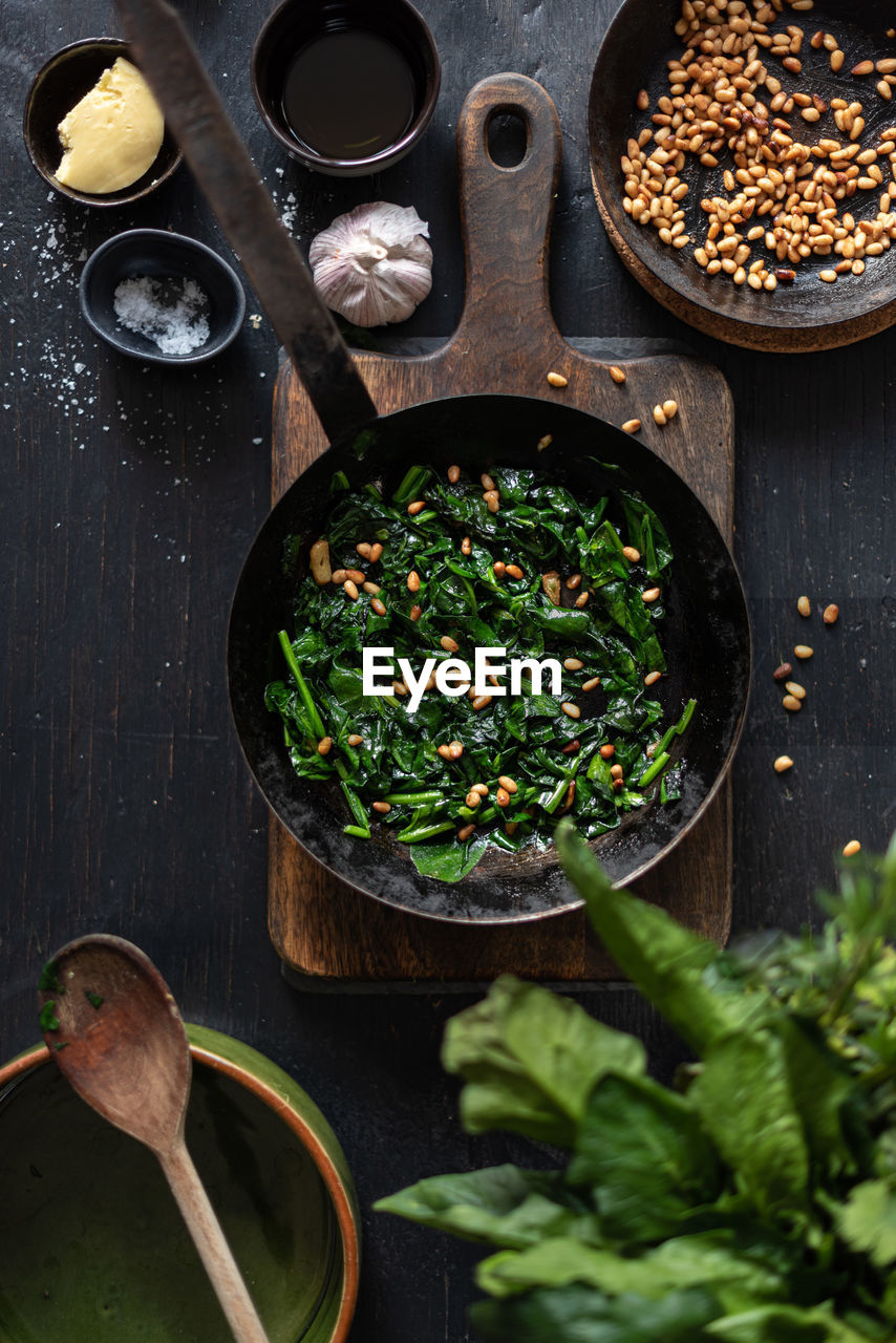 From above of tasty catalan spinach with pine nuts in frying pan served on table in kitchen