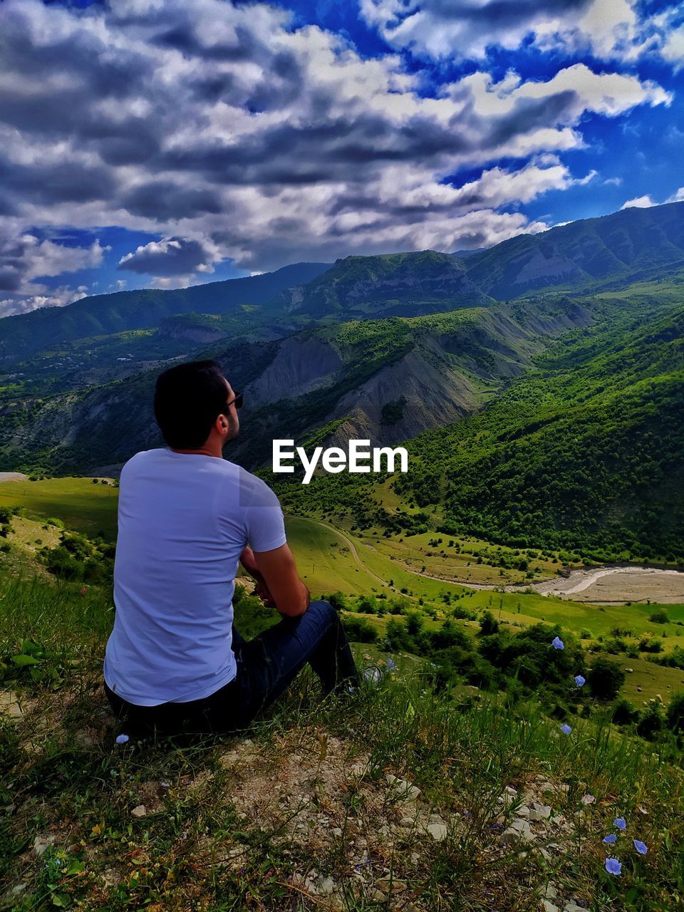 Rear view of woman sitting on mountain against sky