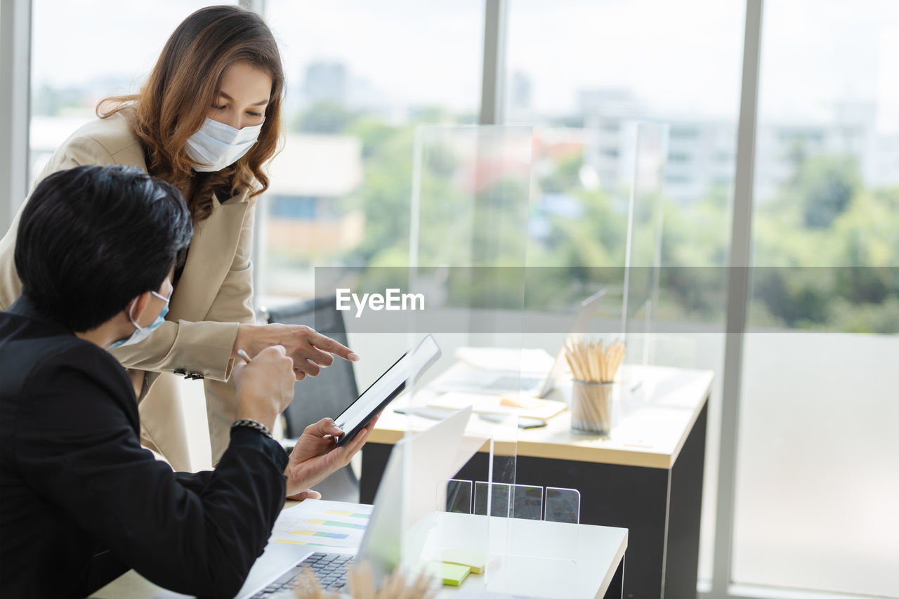 Business persons wearing mask using digital tablet brainstorming in office