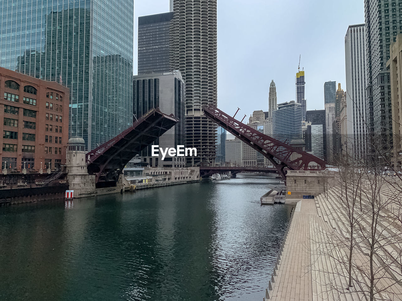 Bridge over river by buildings in city against sky
