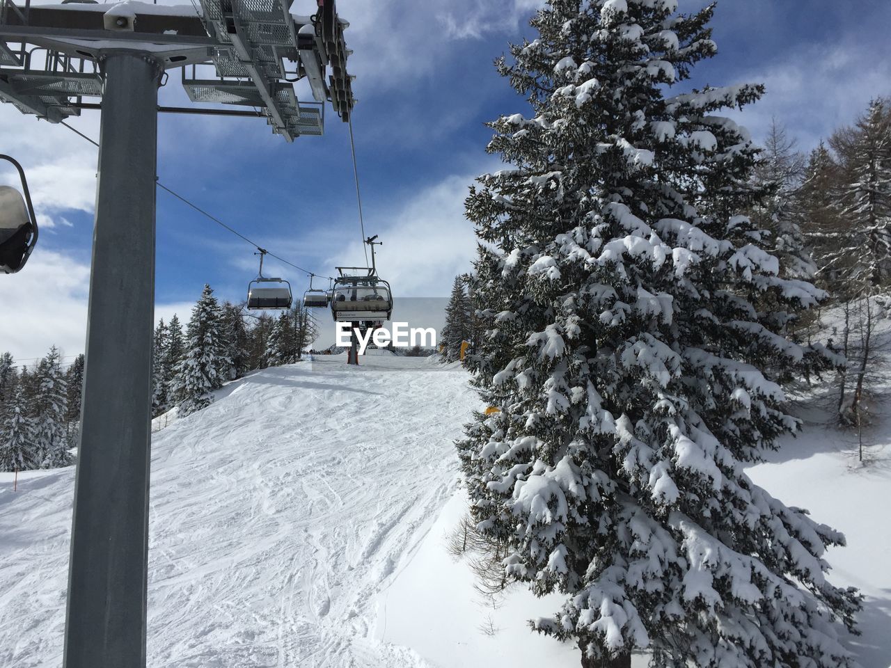 Low angle view of ski lift over snowy field amidst frozen trees against sky