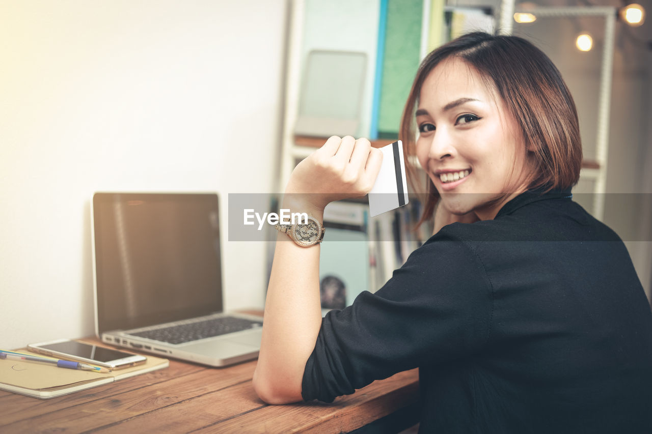 Portrait of smiling businesswoman holding credit card while sitting at table