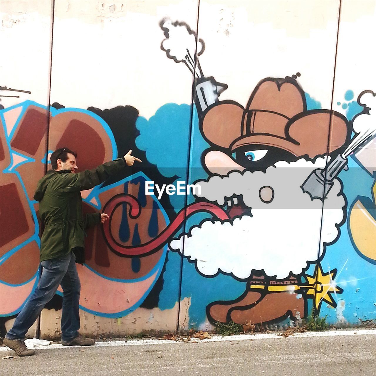 Smiling man pointing finger at mural on wall on street