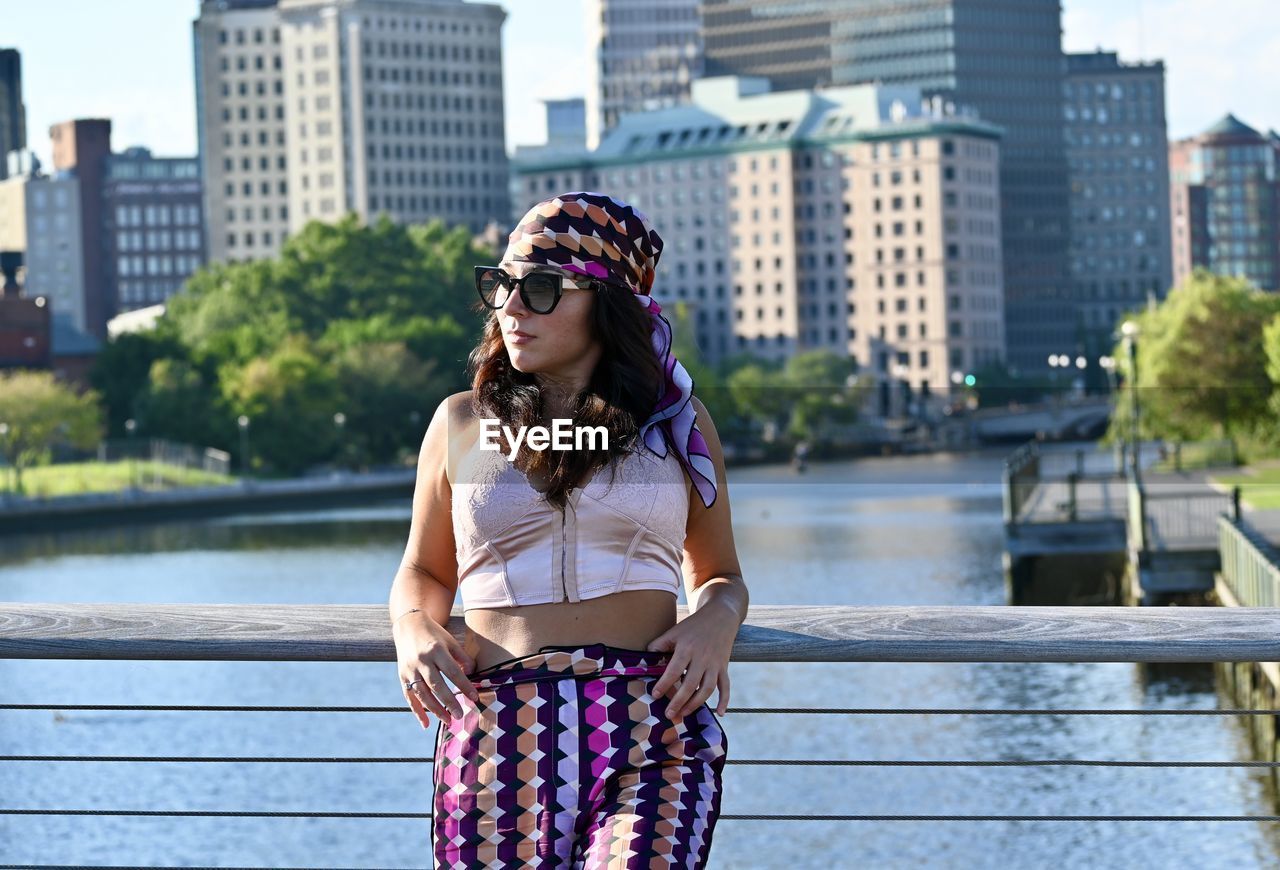 Woman wearing sunglasses looking away standing against buildings