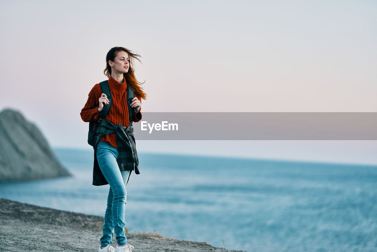 YOUNG WOMAN STANDING AT SEA AGAINST SKY