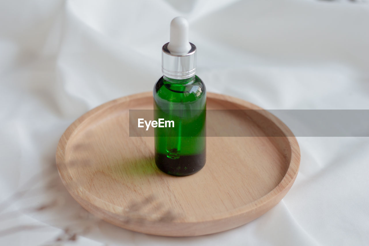 Green dropper bottle serum on wood plate. natural facial essential oil or serum.