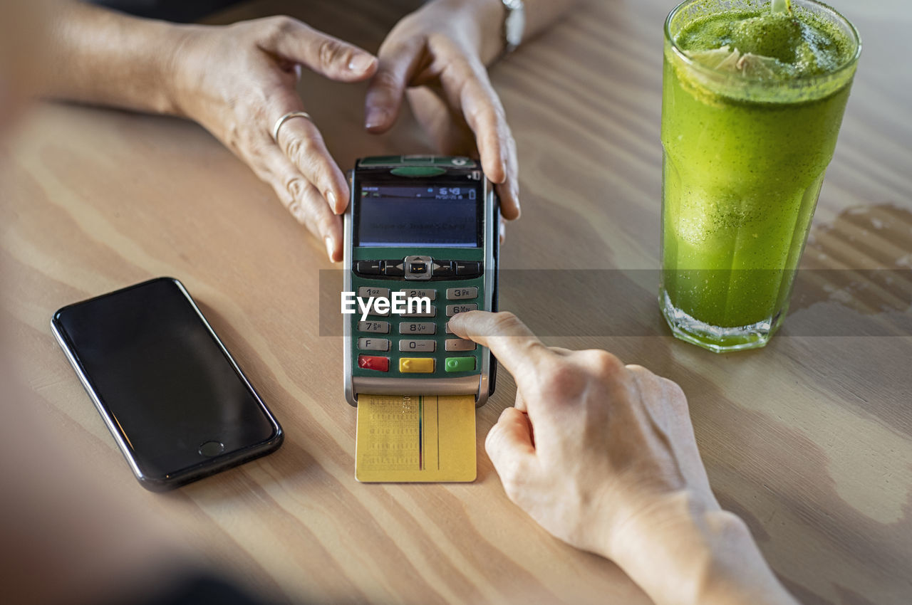 Cropped hands of female customer making credit card payment to owner on wooden table in cafeteria