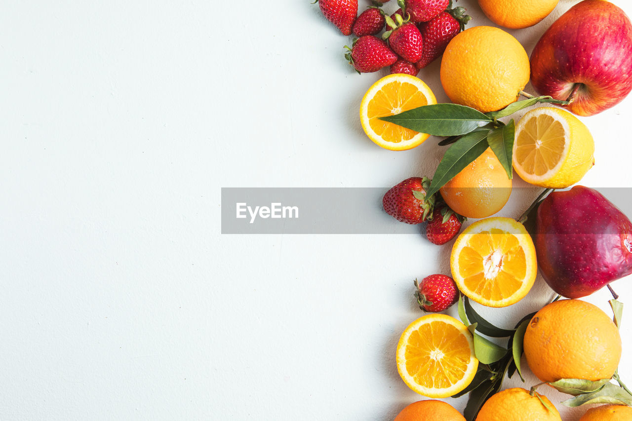 Flat lay of citrus fruits like lime, orange and lemon with leaves on light colored background.