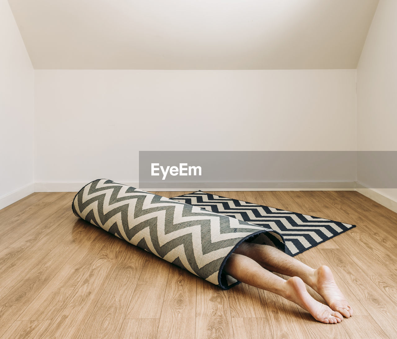Person with bare feet rolled up inside carpet on floor in empty room
