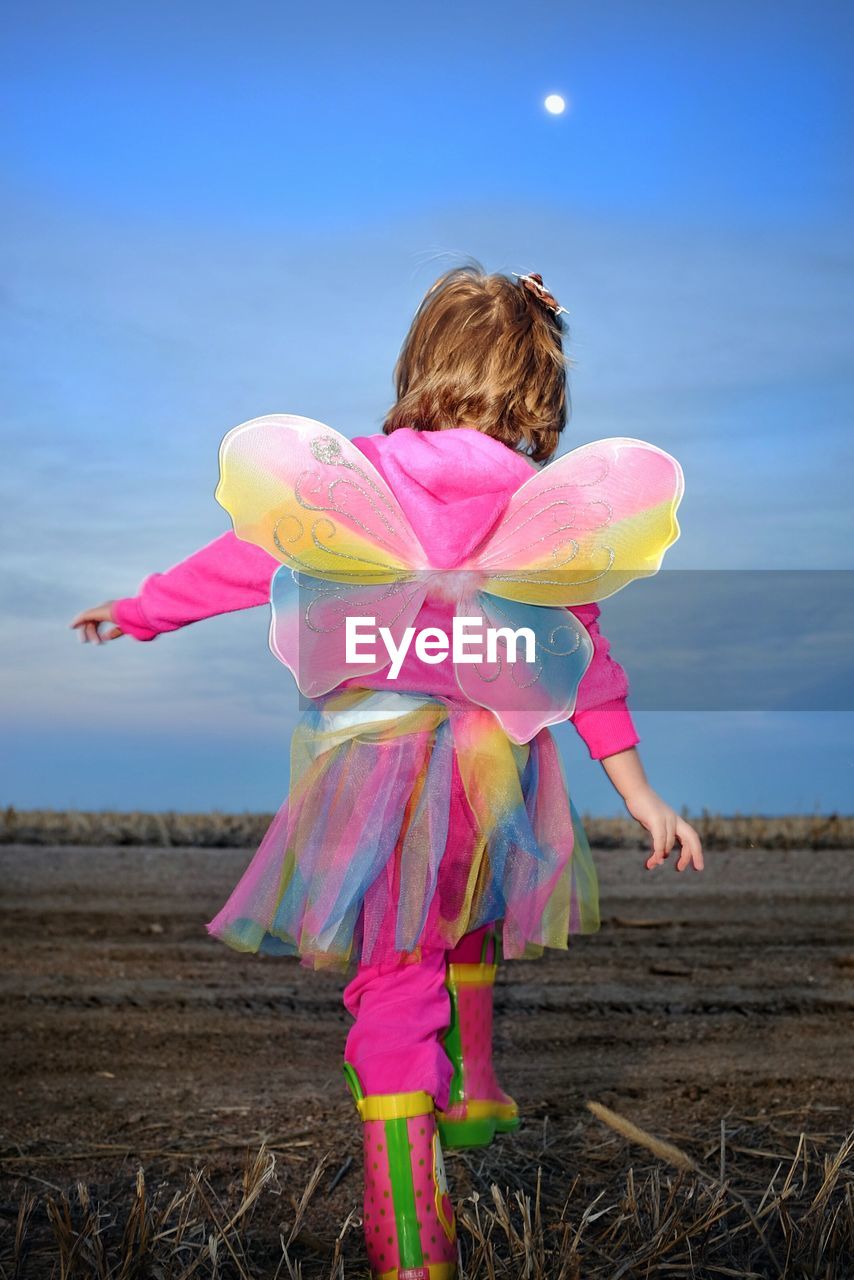 Rear view of girl in colorful costume walking on field against sky