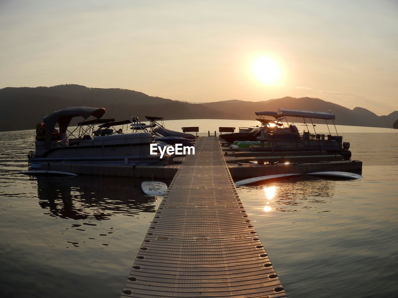 Boats moored on river by mountains against sky during sunset