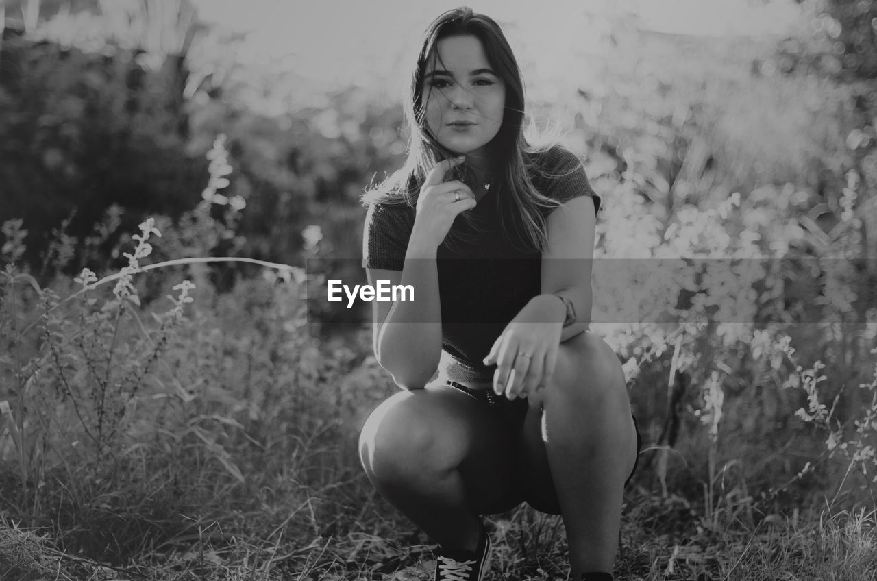 YOUNG WOMAN SITTING ON FIELD BY LAND