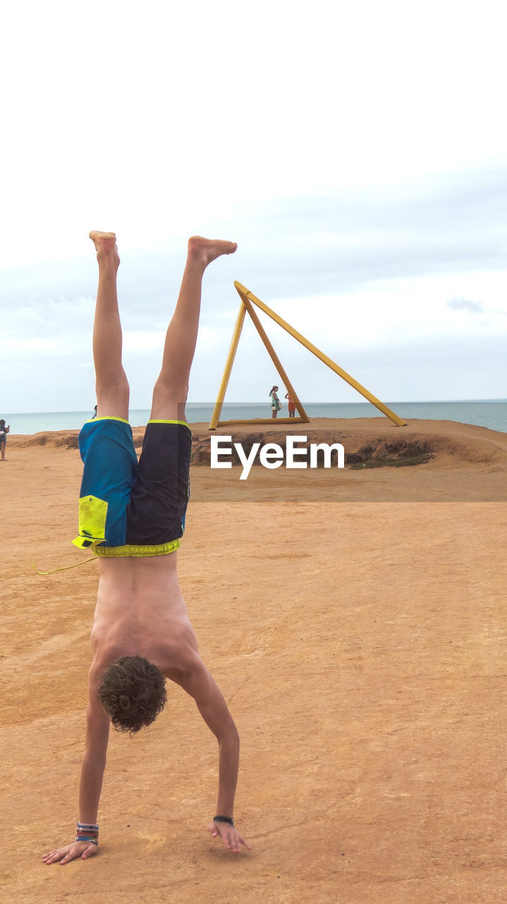 Young man practicing handstand on sand at beach