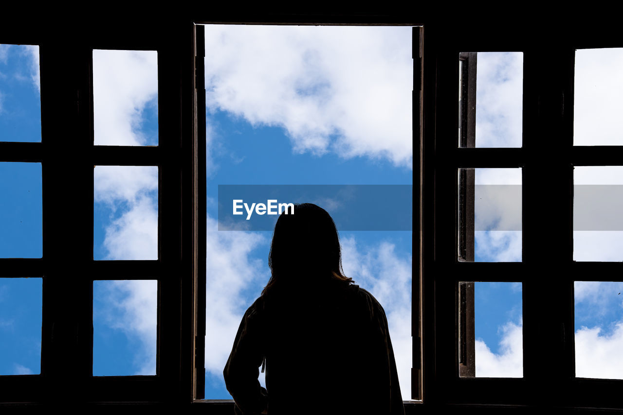 REAR VIEW OF MAN LOOKING THROUGH WINDOW