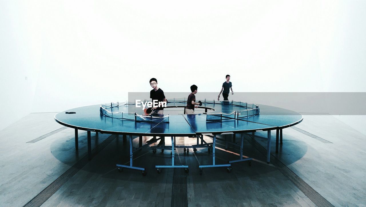 Boys playing ping pong go-round against white background