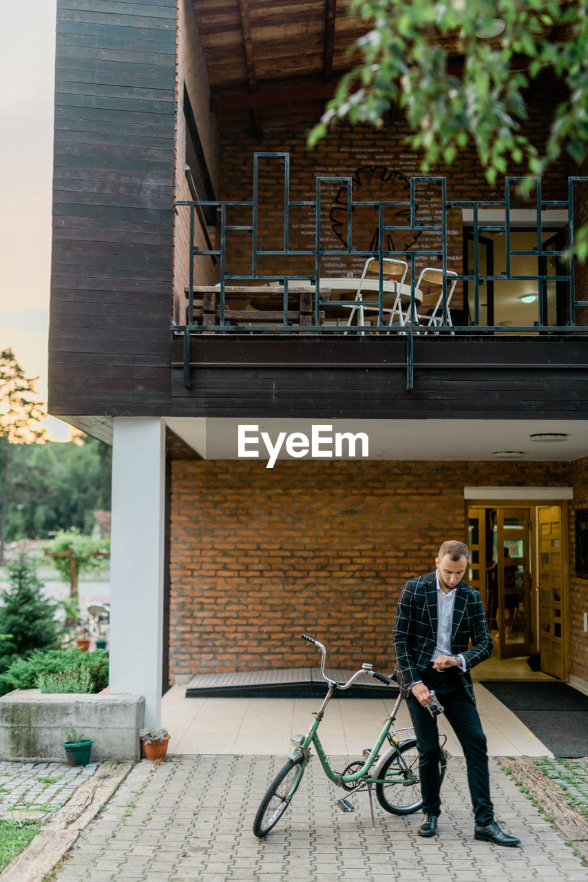 FULL LENGTH OF MAN WITH BICYCLE ON BUILDING