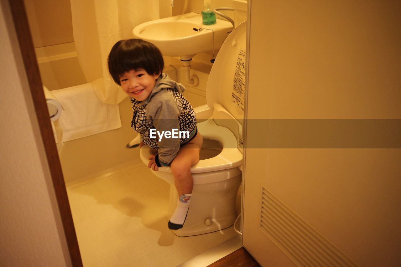 Cute boy sitting on toilet bowl at bathroom