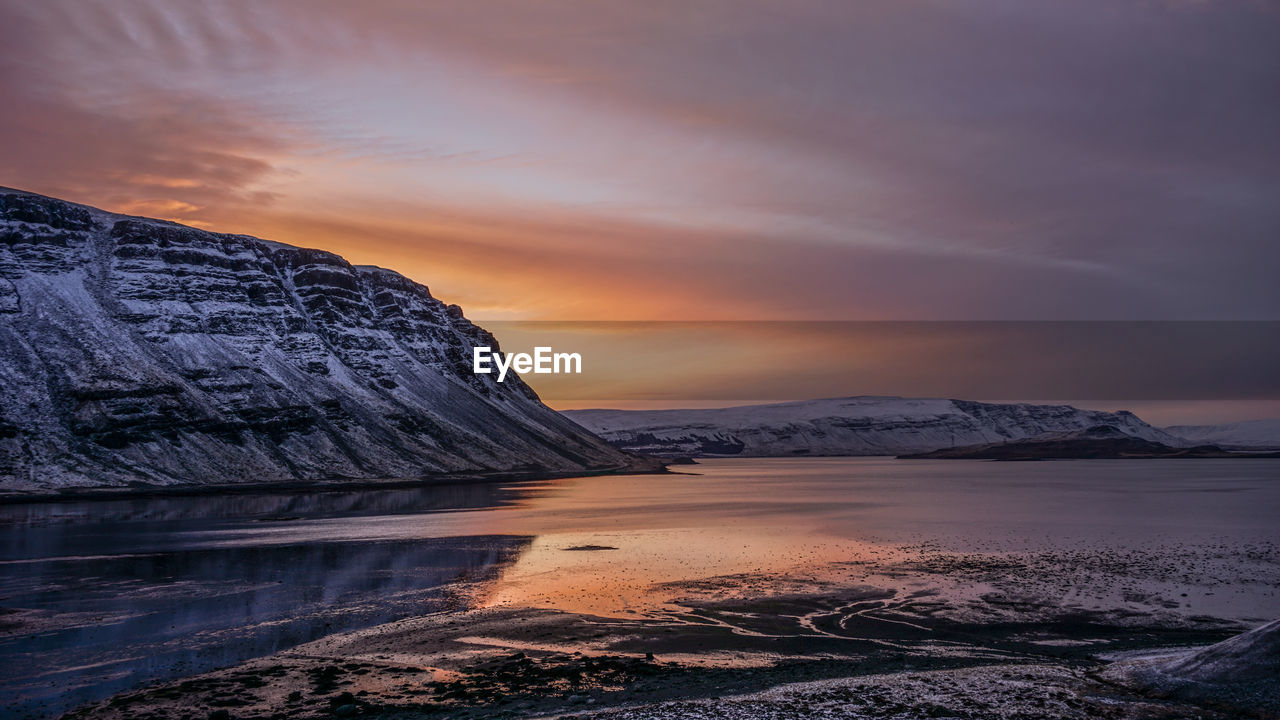 Scenic view of lake by mountains against sky during sunset