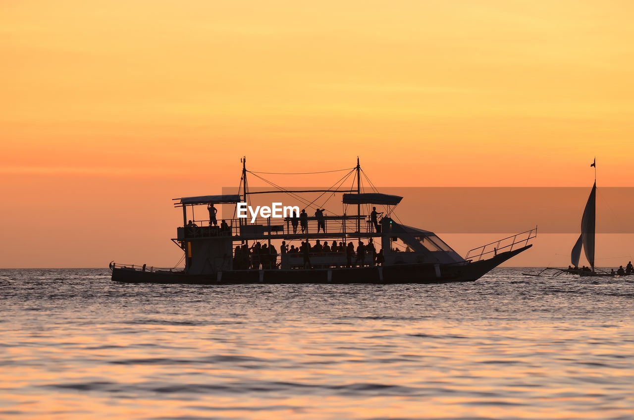 Silhouette ship in sea against orange sky