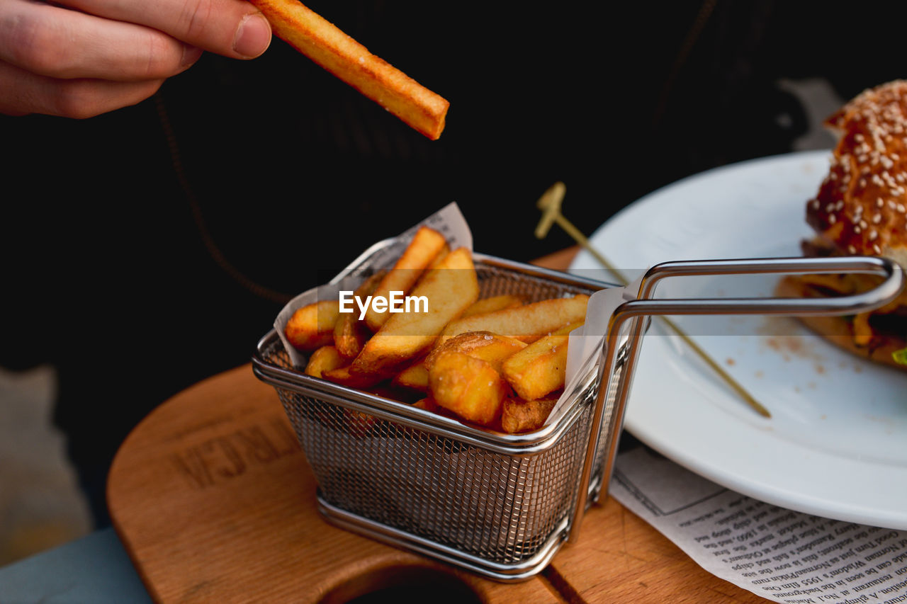 Cropped image of person eating french fries at restaurant