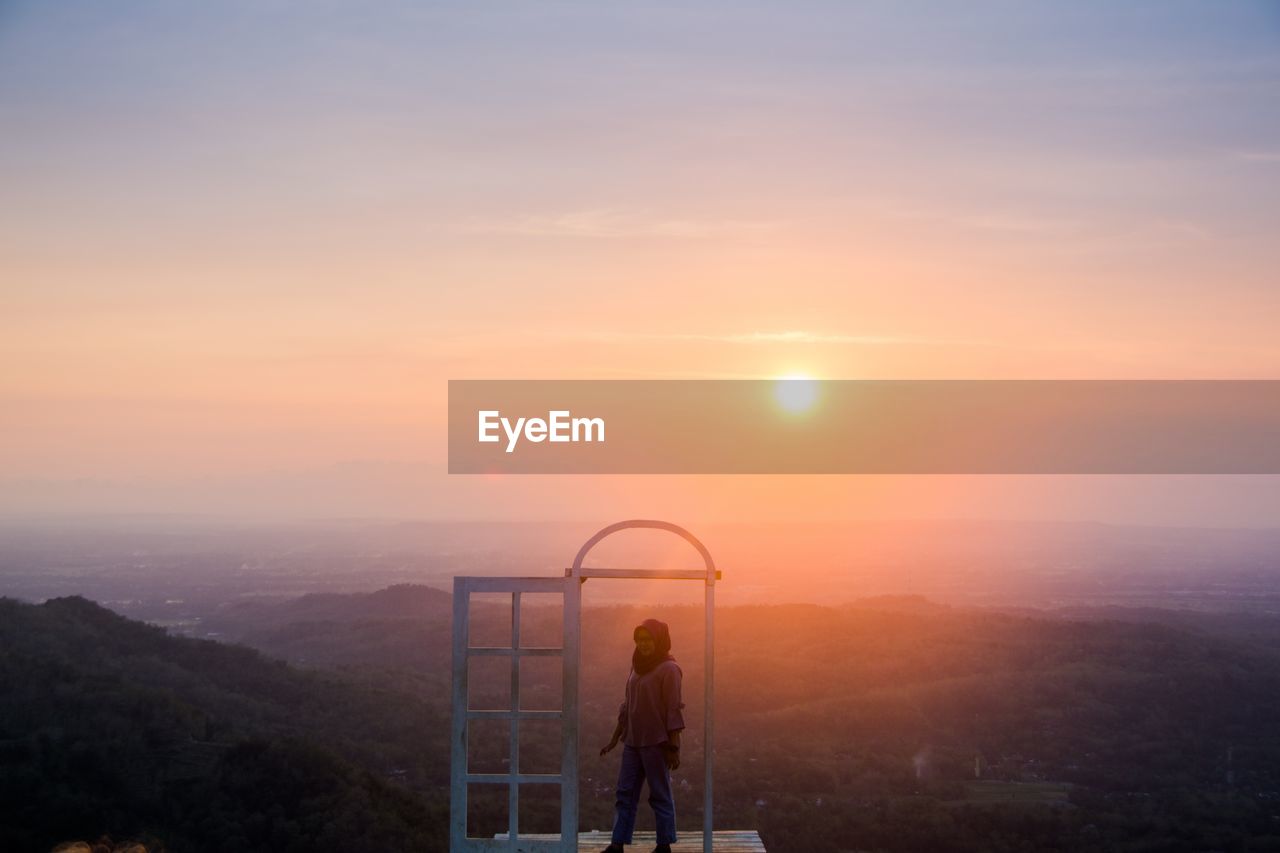 MEN STANDING ON MOUNTAIN AGAINST SKY DURING SUNSET