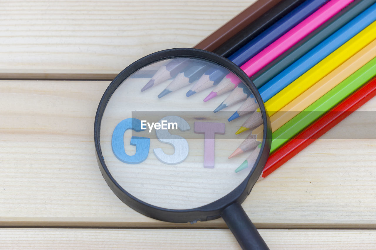 High angle view of colored pencils with magnifying glass on wooden table