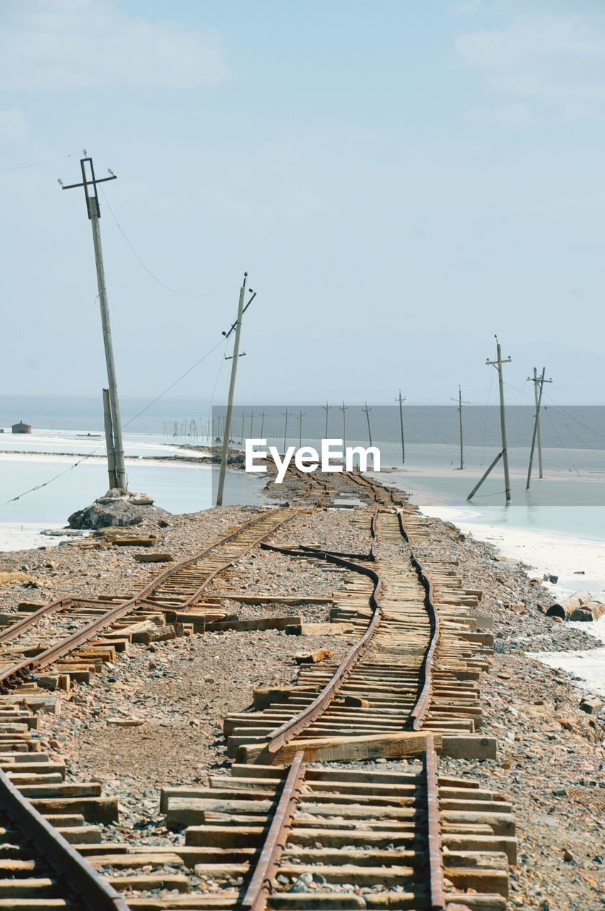 Broken railroad tracks passing by lake against clear sky