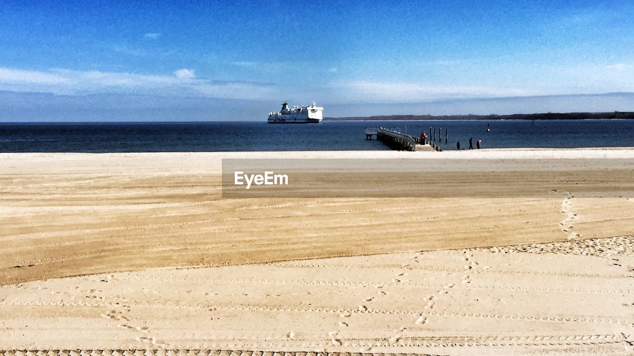 Boat moving on sea in front of sand against blue sky