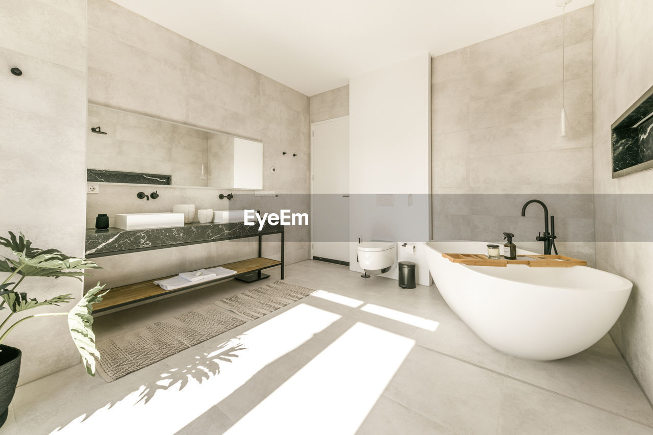 Modern interior of bathroom with white bathtub and ceramic wall mounted toilet and double sinks in minimal style