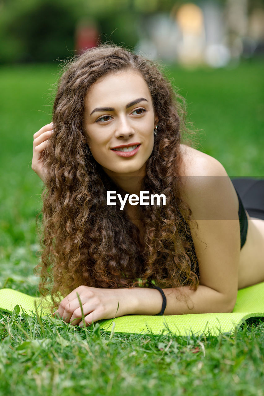 Portrait of young woman lying on front at park