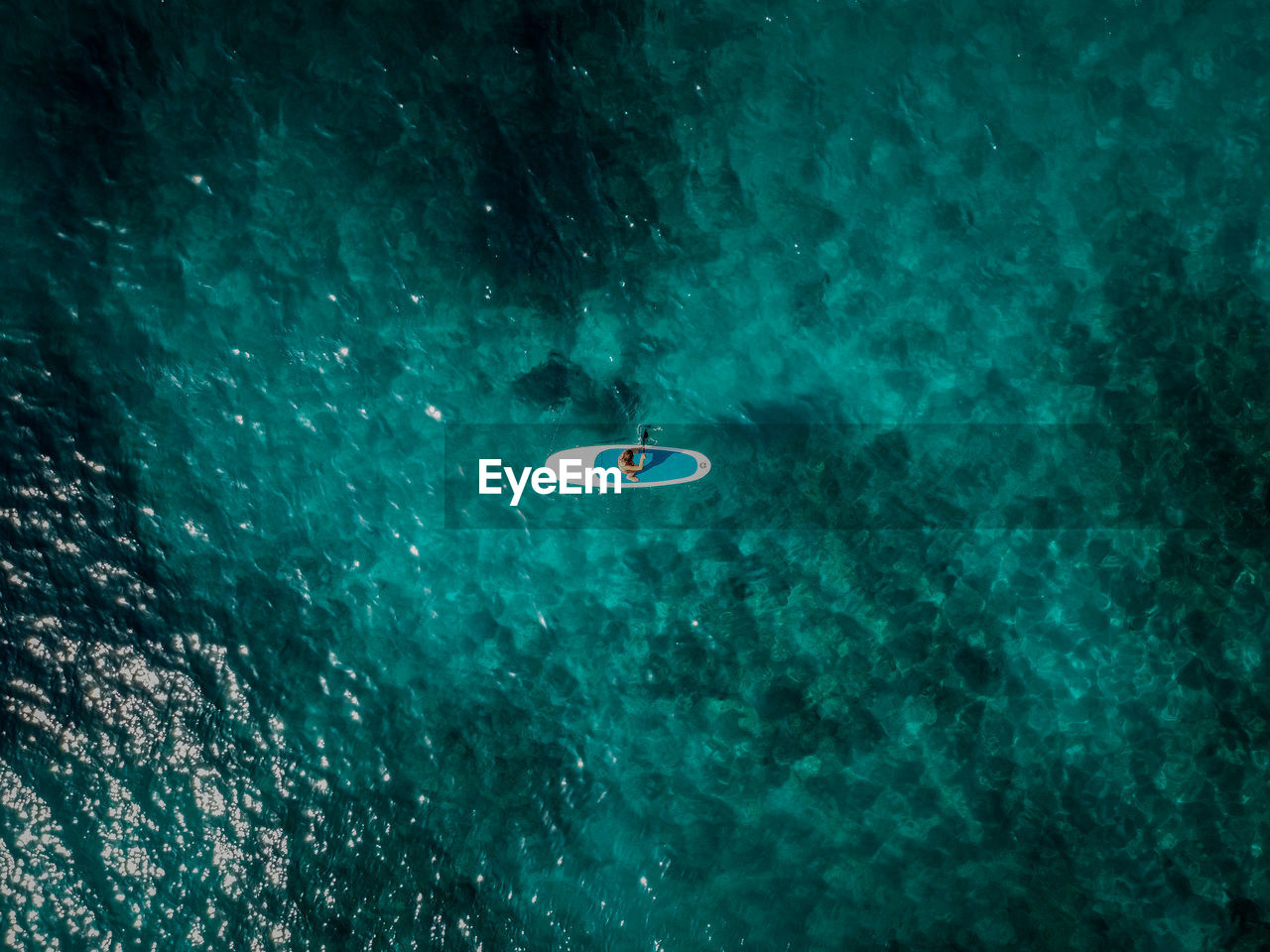 Aerial drone photo of a woman on a standup paddle board in beautiful blue water.