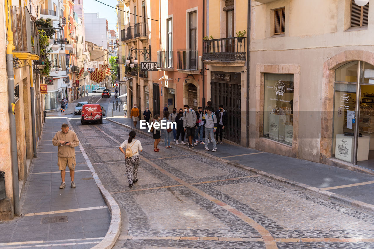 PEOPLE WALKING ON STREET AMIDST BUILDINGS