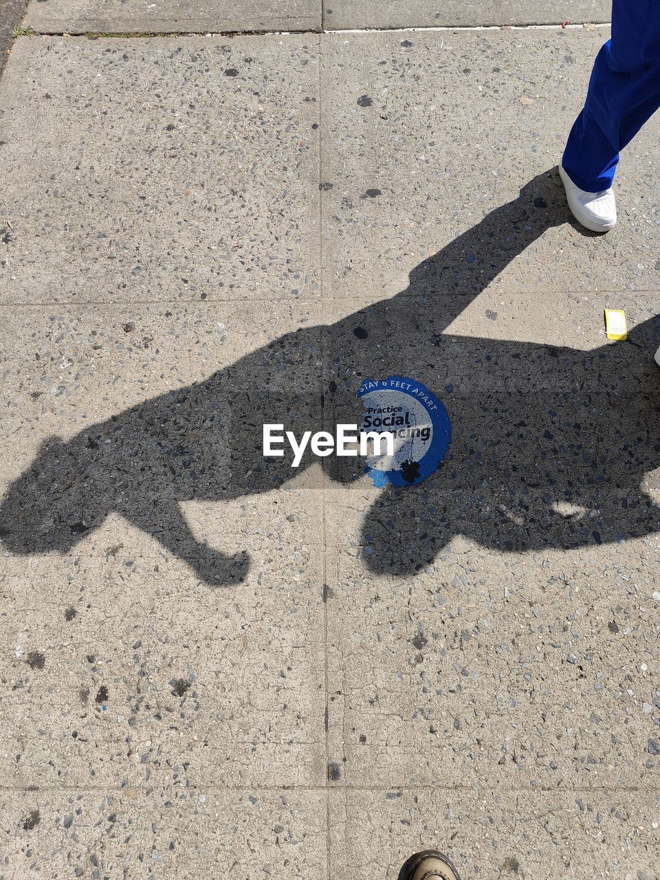 low section, human leg, shadow, shoe, high angle view, one person, sunlight, day, asphalt, footwear, lifestyles, standing, blue, road surface, leisure activity, human limb, limb, men, road, nature, city, street, outdoors, human foot, flooring, sign, sand, floor, footpath, sports, land