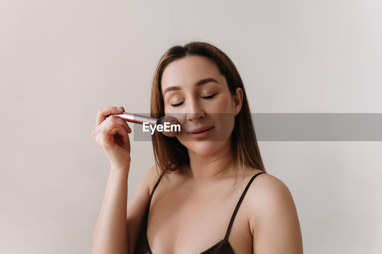 A beautiful natural woman makeup artist preens herself with makeup on a white isolated background