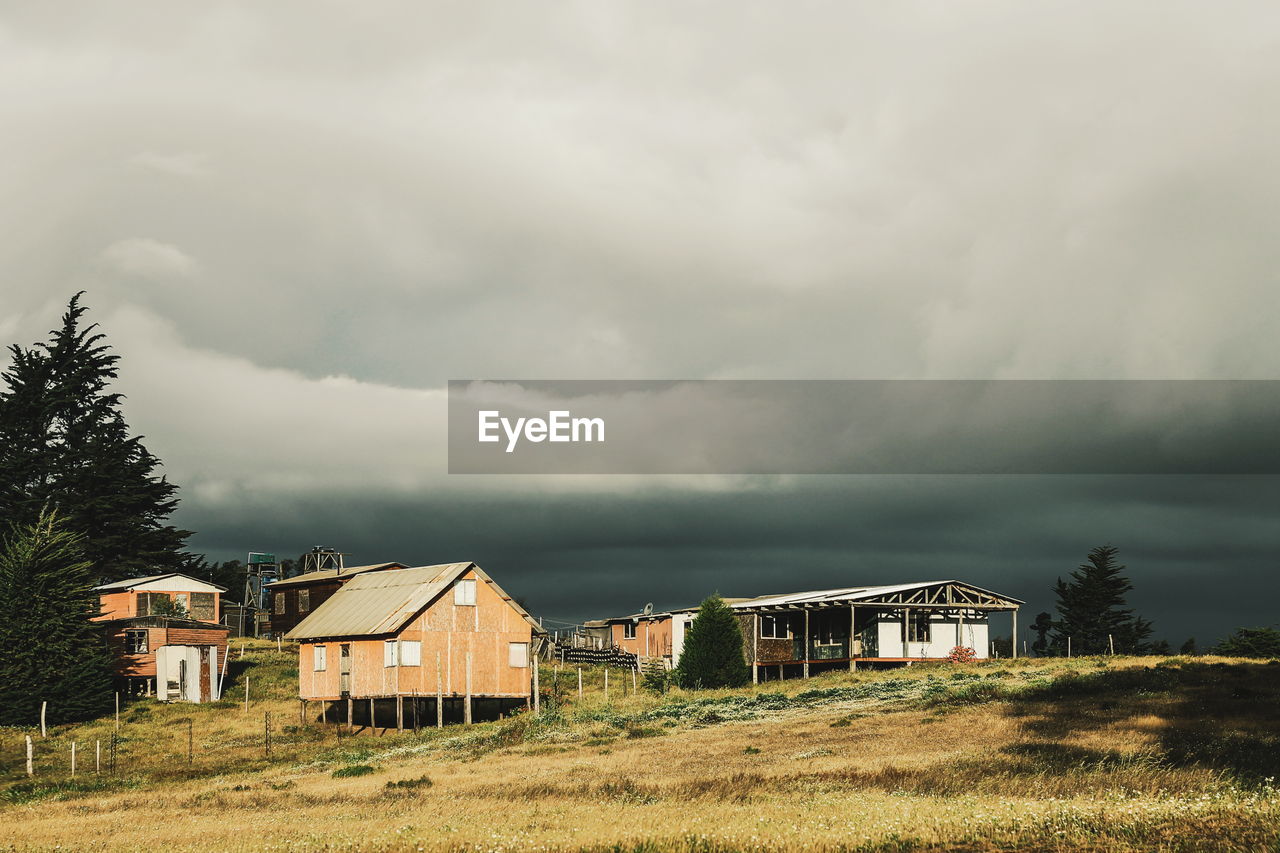 Stilt houses on field against cloudy sky