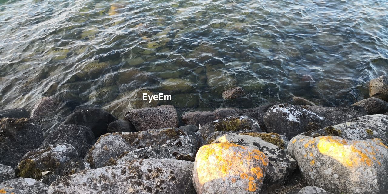 HIGH ANGLE VIEW OF PEBBLES IN SEA