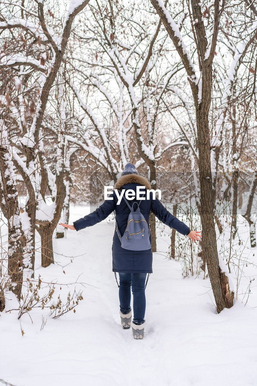 Rear view of woman wearing warm clothing with backpack walking on snow in forest