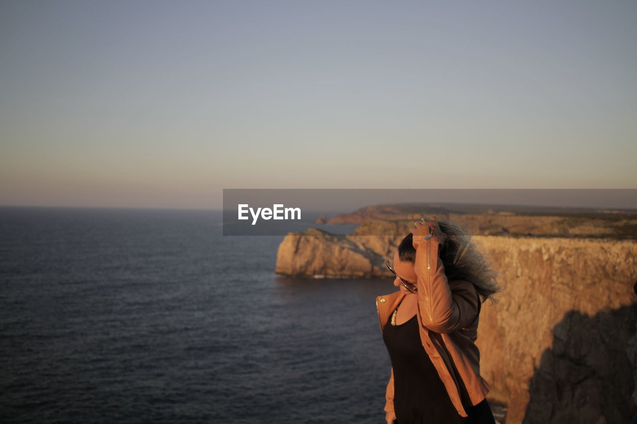 Woman with hand in hair against sea during sunset